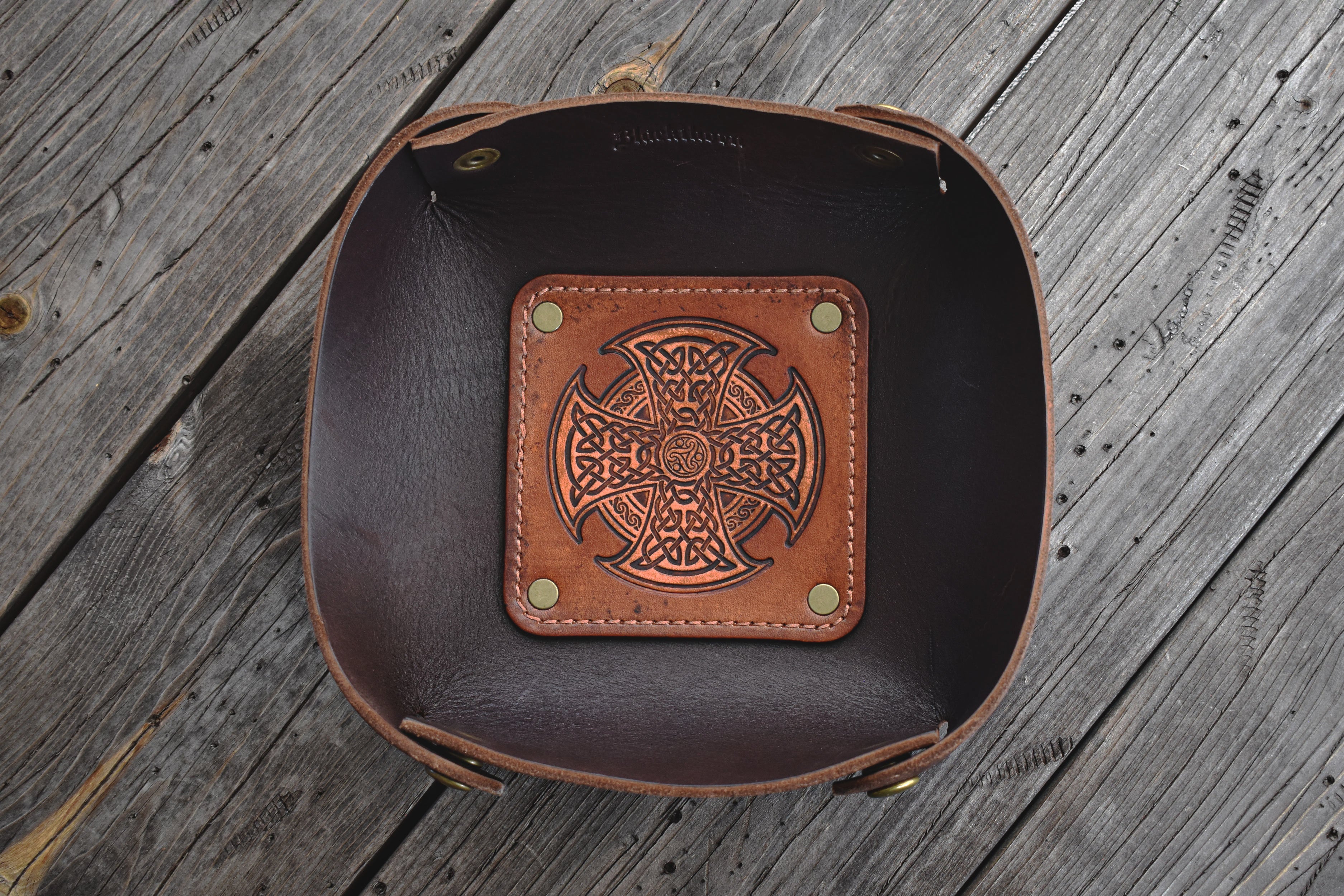 Brown leather valet tray with Celtic knot design on a wooden surface