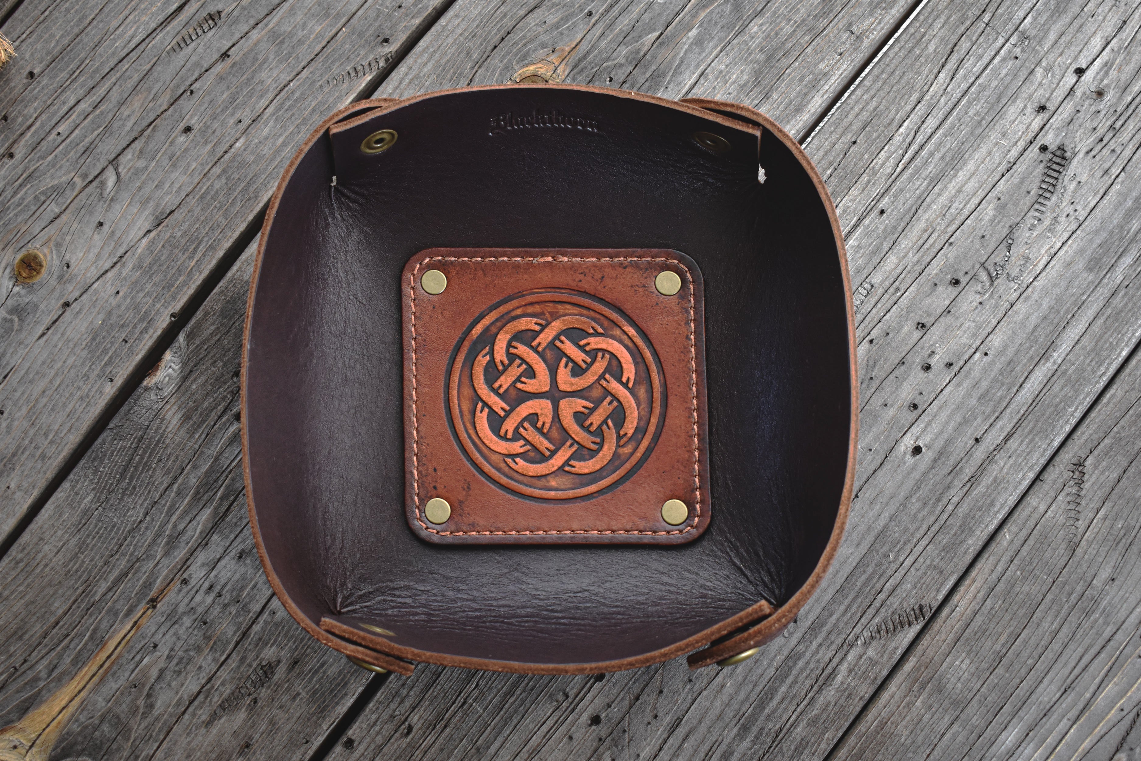 Brown leather valet tray with Celtic knot design on a wooden surface