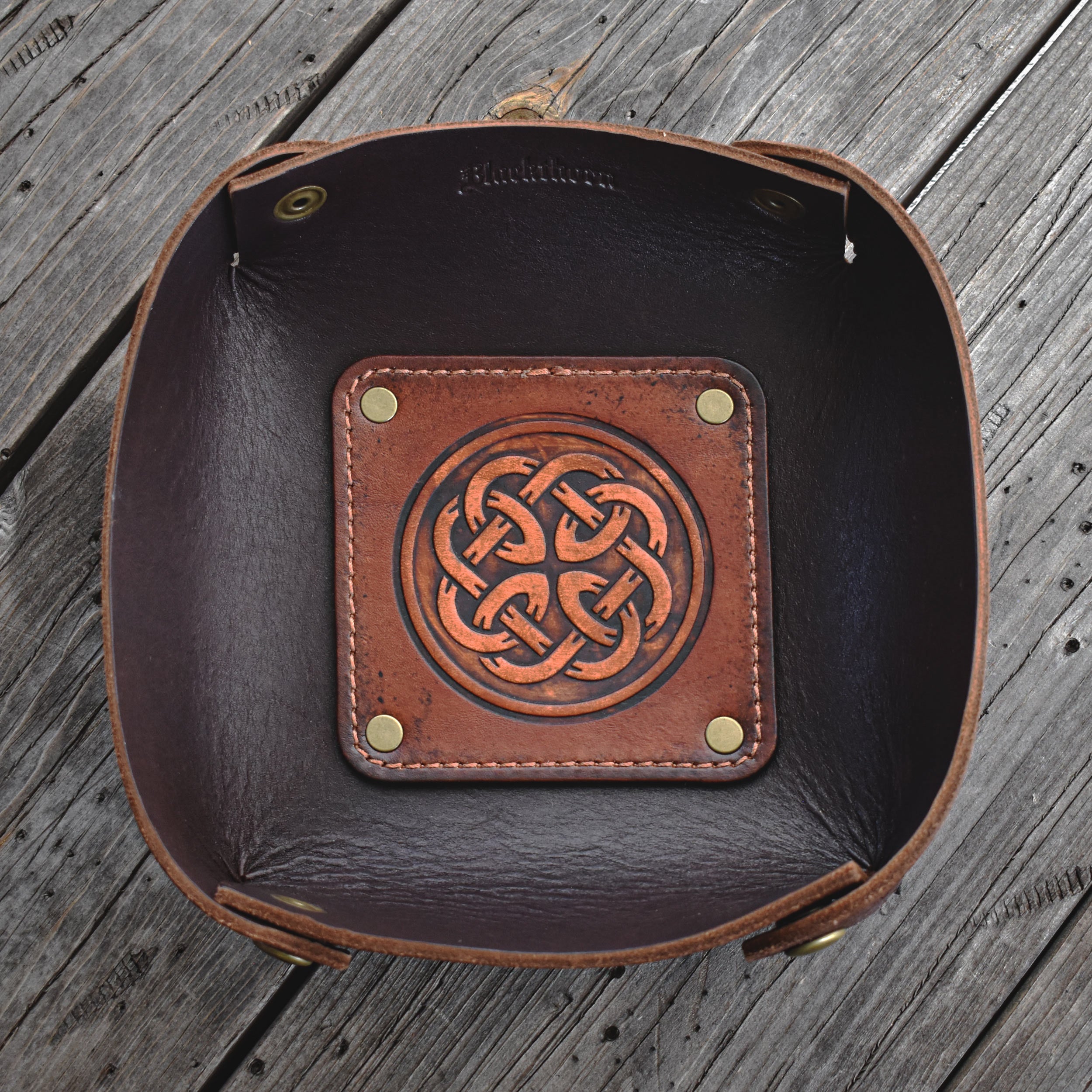 Brown leather valet tray with Celtic knot design on a wooden surface
