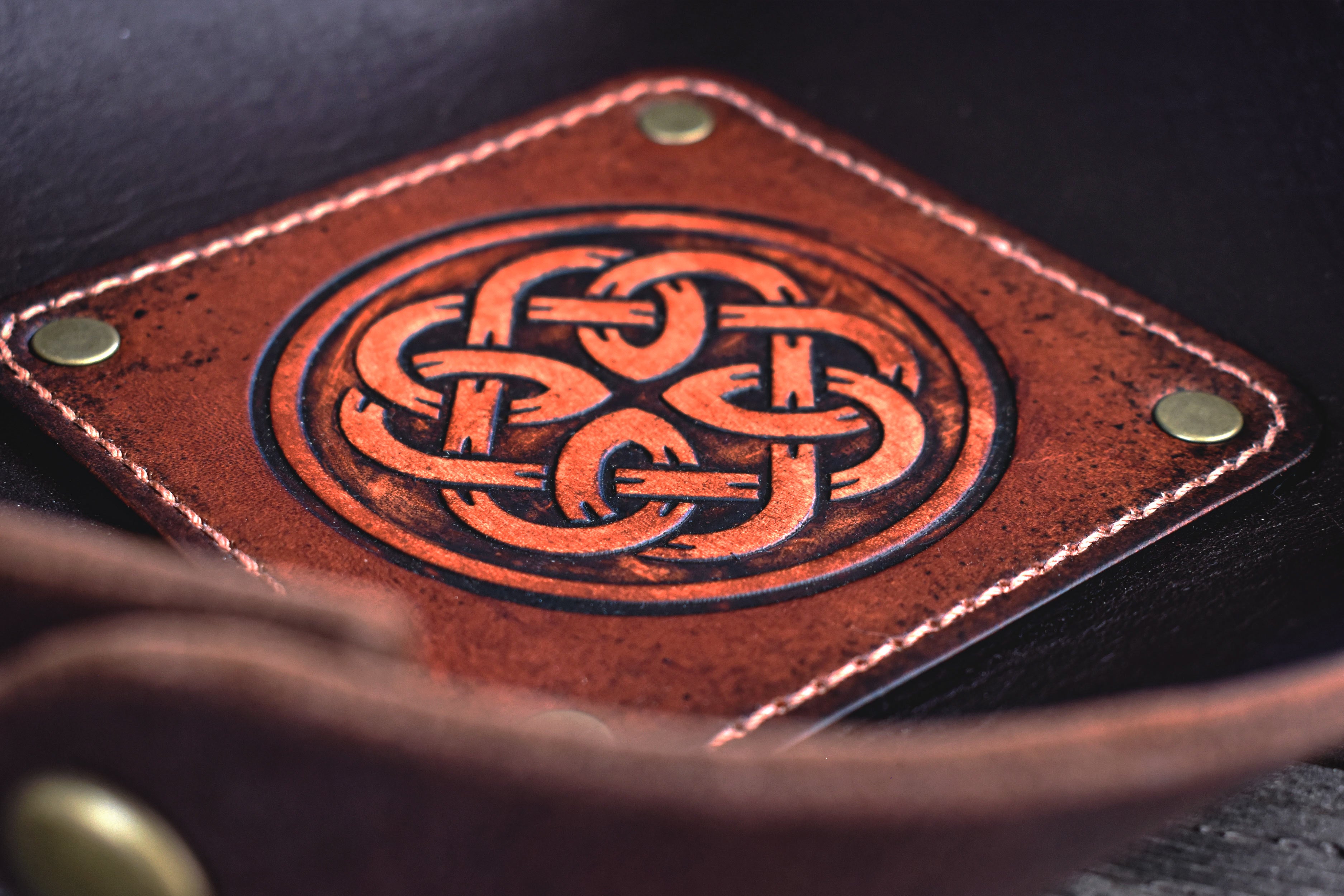 Brown leather valet tray with Celtic knot design on a dark background