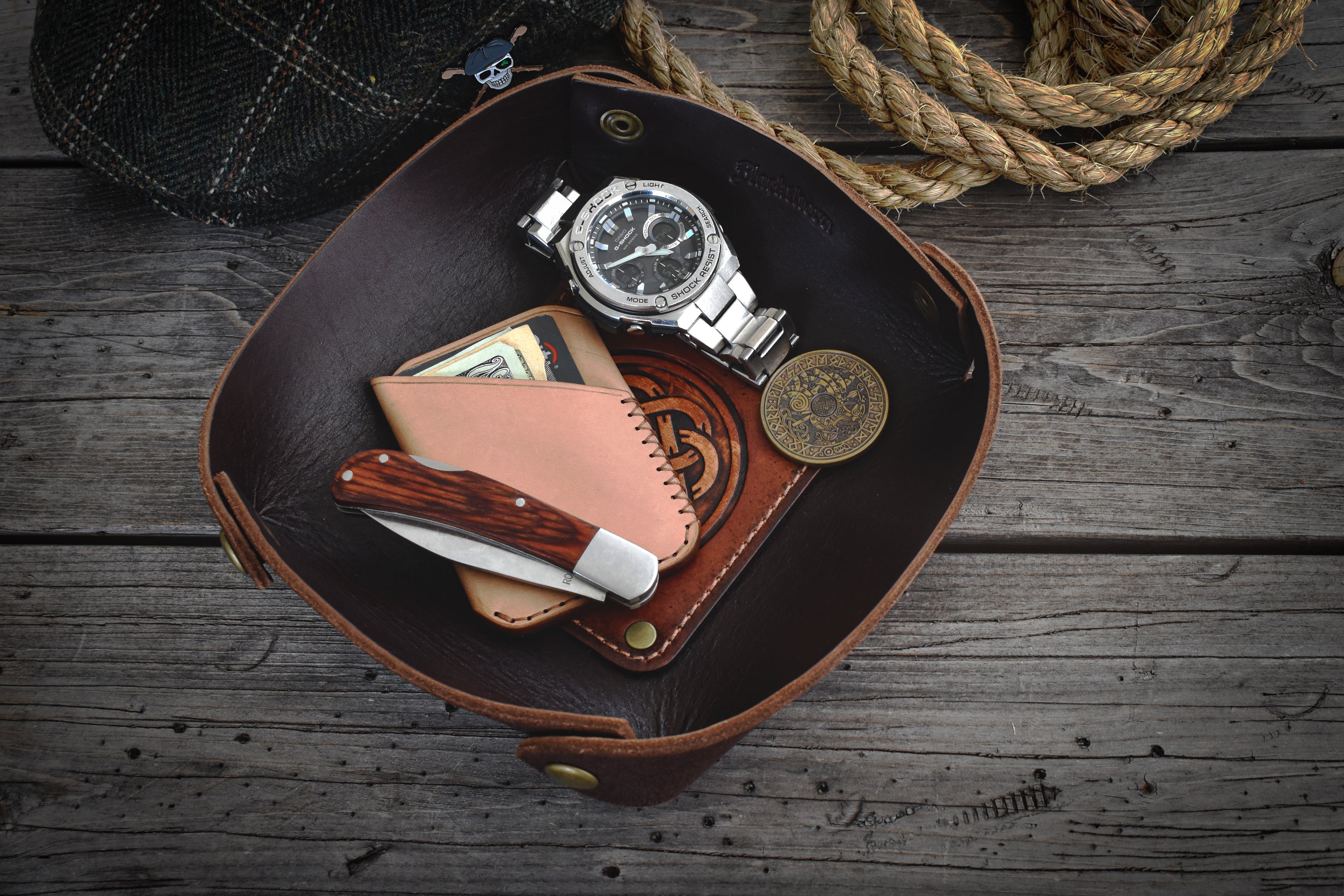 Brown leather valet tray with a watch, knife, and wallet on a wooden surface